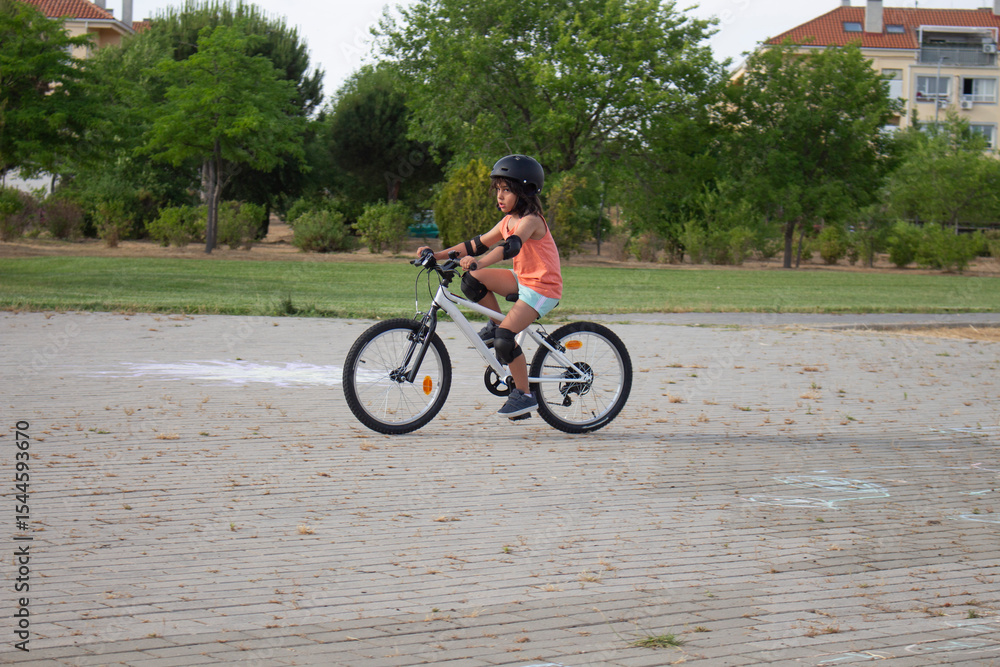 Obraz premium Young girl riding bicycle wearing helmet and protections in a park