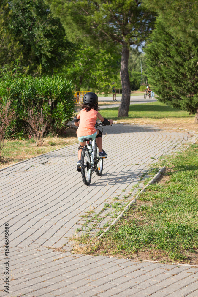 Naklejka premium Girl riding bicycle wearing helmet and protections in a park