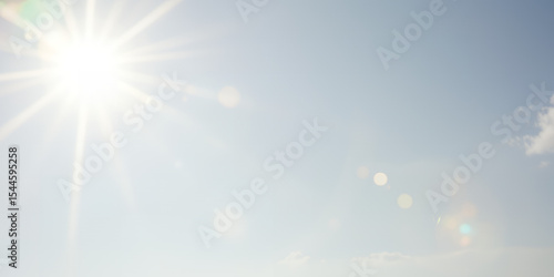 A bright sun shining in a pale blue sky with a few clouds and lens flares visible today