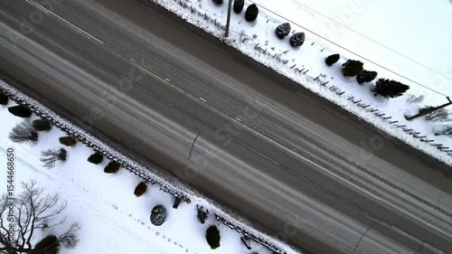 Top-down View of a Road Cutting Through Snowy Landscape. Top-down view of a quiet road dividing a snow-covered field, bordered by trees and winter shadows, ideal for seasonal or nature themes