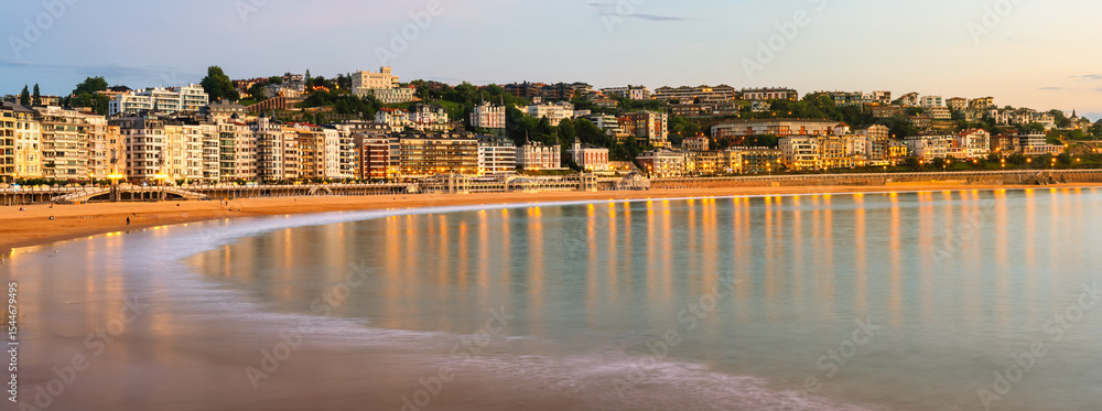 Naklejka premium Great panoramic view of La Concha Bay in San Sebastian as the sun sets and the city lights come on