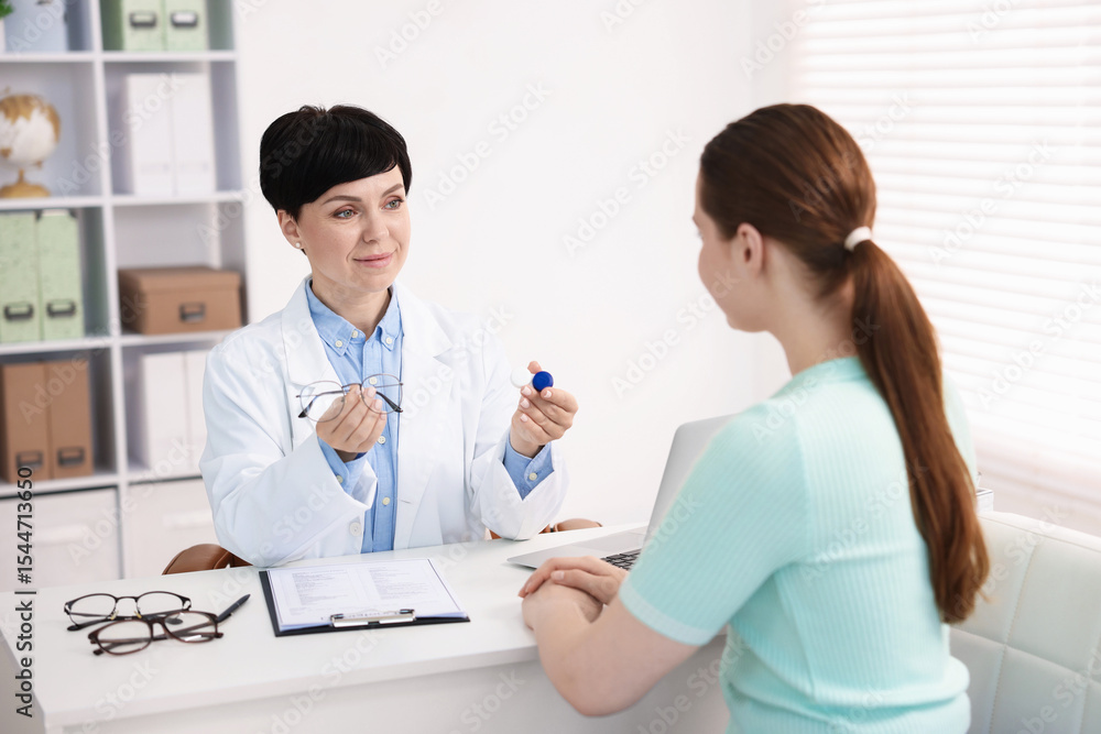 Ophthalmologist giving contact lenses and glasses to patient at table in office Ophthalmologist giving contact lenses and glasses to patient at table in office