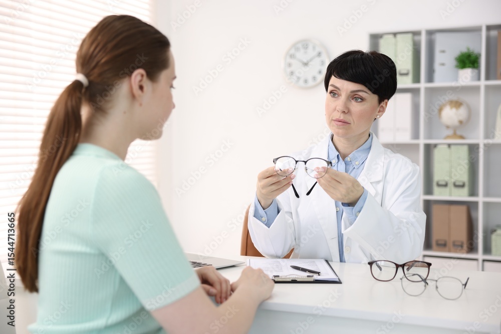 Fototapeta premium Ophthalmologist giving glasses to patient at white table in clinic