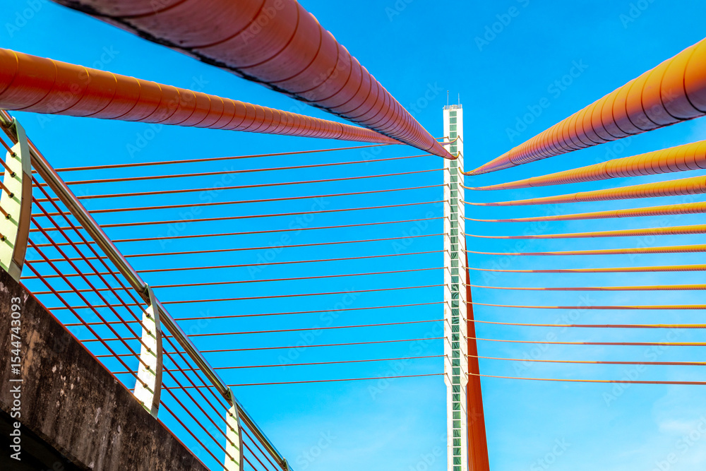 Fototapeta premium Modern architectural bridge design with vibrant cables against blue sky