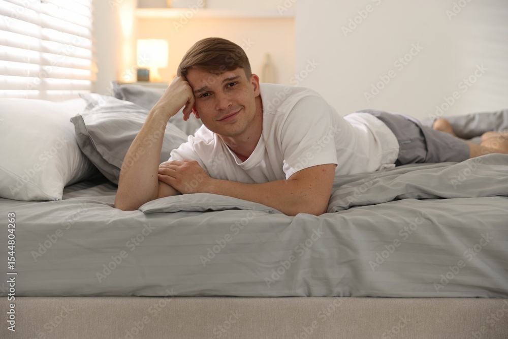 Young man lying on bed with soft mattress at home Young man lying on bed with soft mattress at home