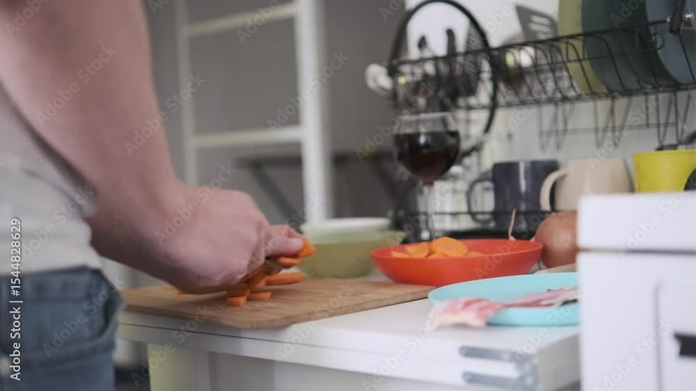 Man slicing carrot on wooden cutting board, preparing fresh ingredients at home kitchen table Man slicing carrot on wooden cutting board, preparing fresh ingredients at home kitchen table
