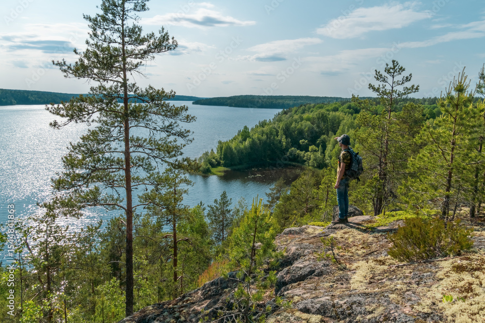 Obraz premium The tourist man standing at edge a rock and looking into the distance at the lake. The concept of win travel.