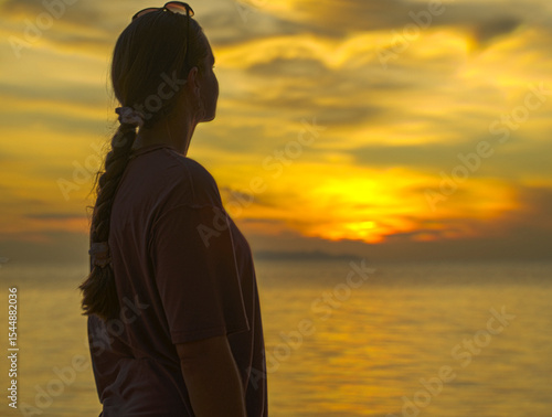 Woman with Braided Hair Looking at the Sunset Over the Ocean from the Beach Captured from Side Angle with Warm Lighting