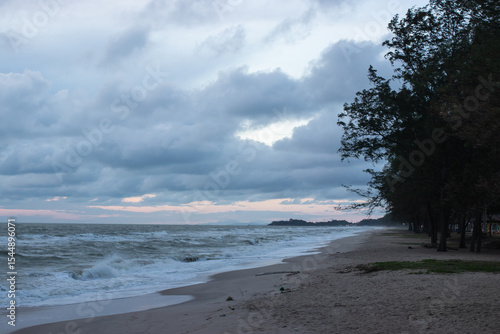Wallpaper Mural A quiet beach with strong waves under a cloudy sky in the early evening, with pine trees lining the coast and soft light peeking through the clouds Torontodigital.ca