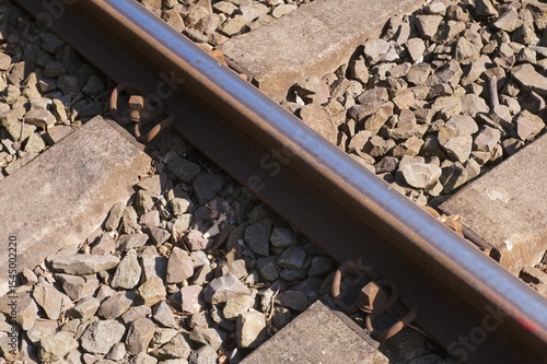 Obraz na plátně Rusty rail fastened to concrete sleepers with gravel ballast in sunlight