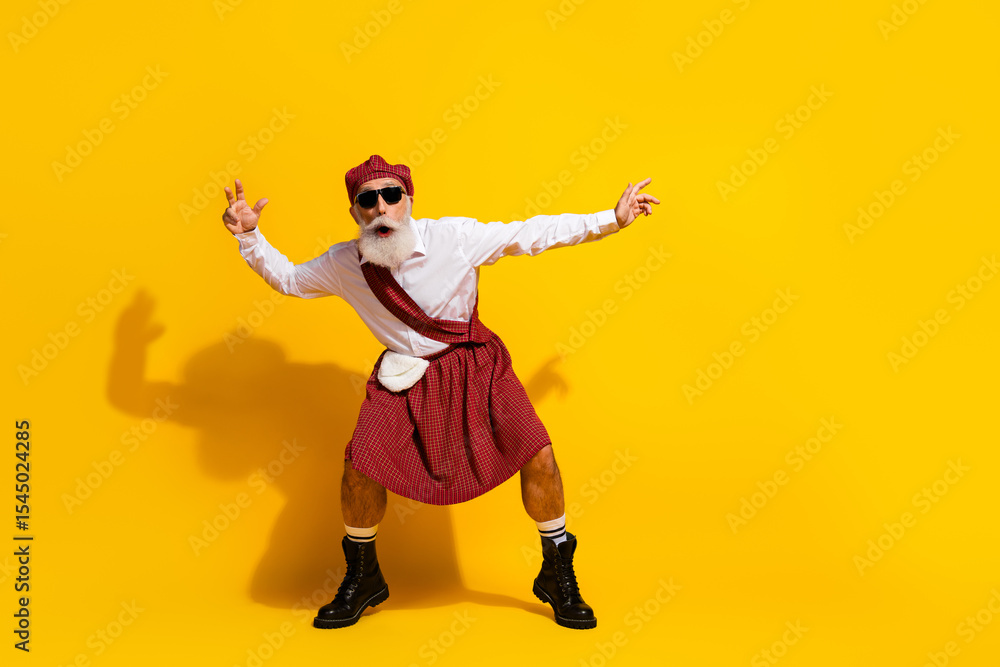 Stylish elderly man in traditional Scottish attire posing with cheerful gestures against a vibrant yellow backdrop Stylish elderly man in traditional Scottish attire posing with cheerful gestures against a vibrant yellow backdrop