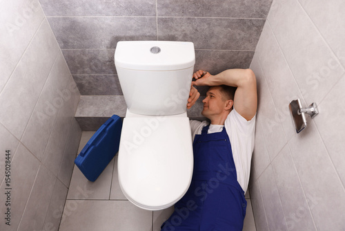 Professional plumber fixing toilet bowl in restroom, above view