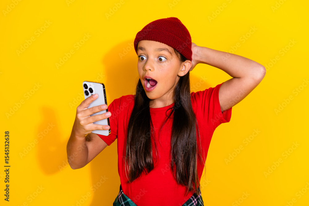 Surprised Young Girl Wearing Red Beanie Holding Smartphone Against Yellow Background in Casual Outfit Expressing Emotion Surprised Young Girl Wearing Red Beanie Holding Smartphone Against Yellow Background in Casual Outfit Expressing Emotion
