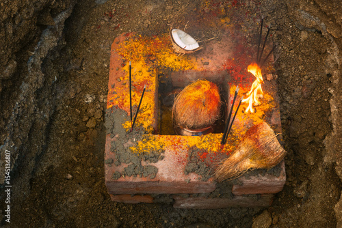 A traditional South Indian Bhoomi Puja setup featuring a lit camphor fire, coconut, turmeric, red powder (kumkum), and ceremonial bricks. This sacred ritual is performed to seek blessings from Mother 