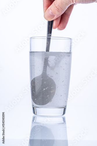 Collagen or medicinal powder is stirred with a spoon in a glass of water on a white background.