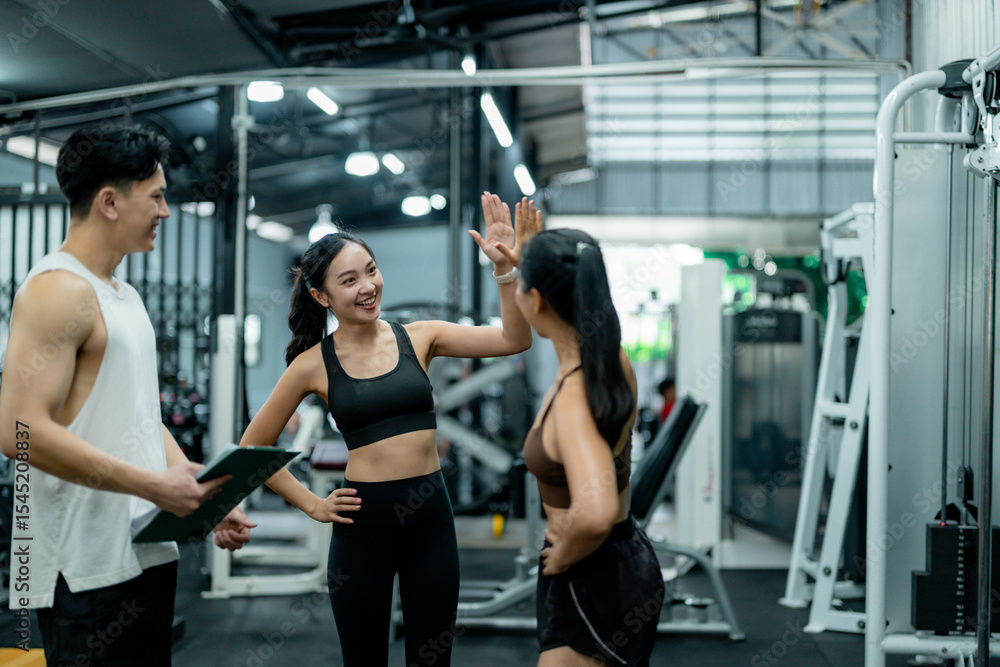 Obraz premium Personal trainers giving high five to client after successful workout in gym