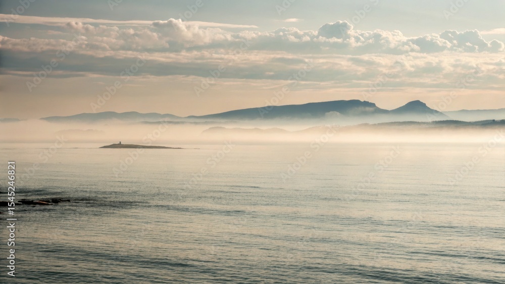 Fototapeta premium Misty morning over calm ocean with distant mountains in background 