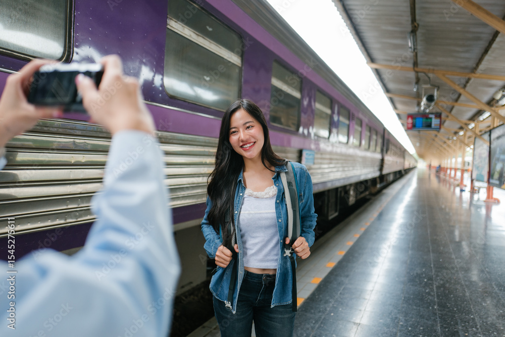 Fototapeta premium Photographer taking pictures of happy tourist woman posing in a train station before boarding