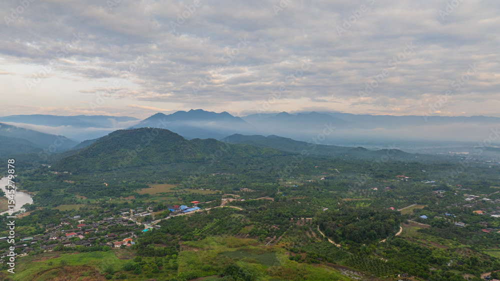 Fototapeta premium A stunning aerial view of a winding river flowing through a vast rural landscape at dawn. The soft morning light and misty atmosphere create a tranquil and picturesque scene, with scattered villages