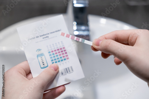 Hands holding a water hardness test strip with comparison chart, evaluating home water quality for shower filter effectiveness and personal health management