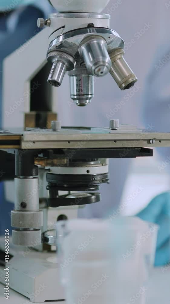 Close-up of doctor scientist worker in white lab uniform examining treatment vaccine on microscope in medical office laboratory. Close-up of doctor scientist worker in white lab uniform examining treatment vaccine on microscope in medical office laboratory.