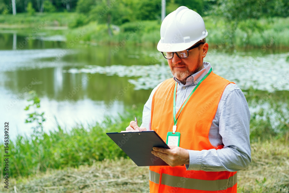 Fototapeta premium Male forestry inspector studying the condition of trees near water in the forest. Ecologist's work. Conducting environmental monitoring.