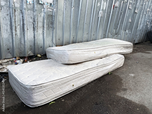 Two old white dirty mattress left on the street by the metallic fence
