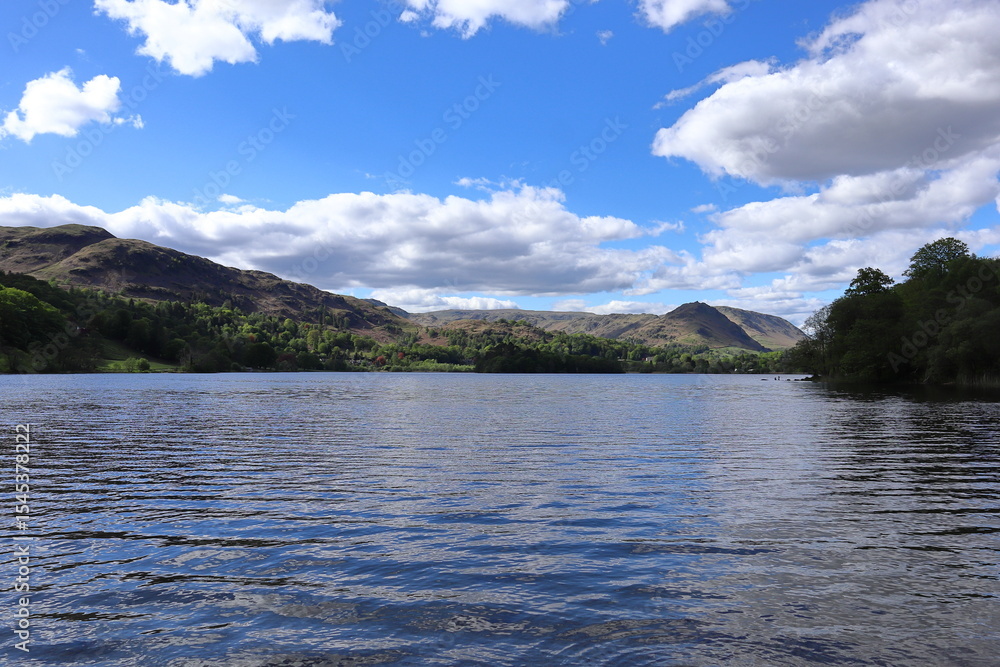 Panorama of Grasmere Lake with calm water and surrounding hills under a partly cloudy blue sky. Lake District, England, UK. Panorama of Grasmere Lake with calm water and surrounding hills under a partly cloudy blue sky. Lake District, England, UK.