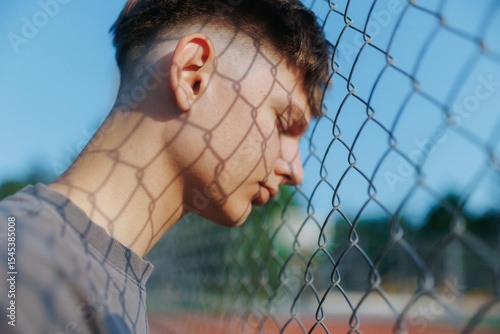 Teen boy leaning on a fence with shadows casting across his face