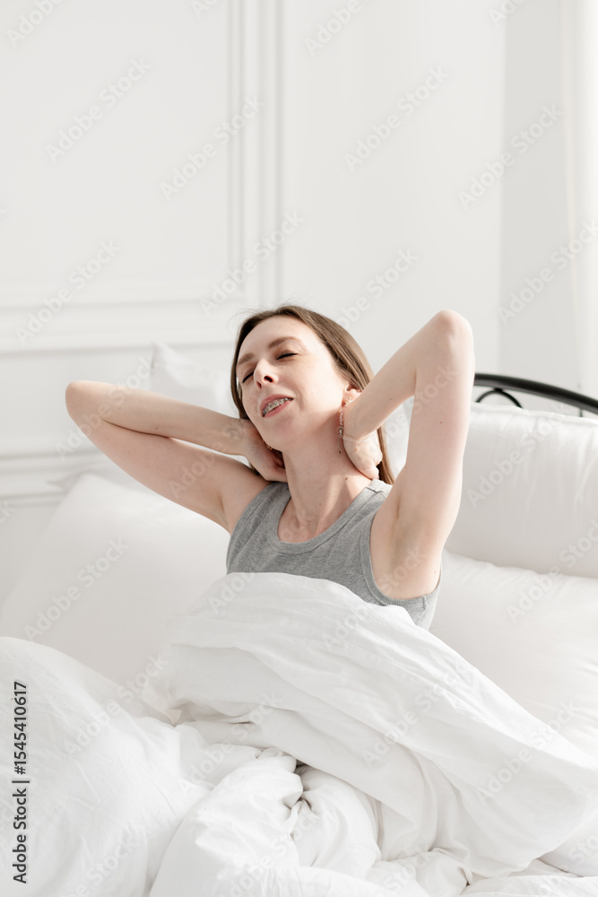 Young and beautiful woman sits on a bed with white bed linen and stretches after sleep. Young and beautiful woman sits on a bed with white bed linen and stretches after sleep.