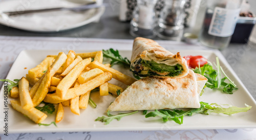 Foto Fresh tortilla wrap served with golden fries and arugula on a white plate close-up