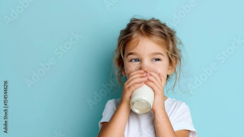 Adorable little girl drinking milk from a glass on blue background