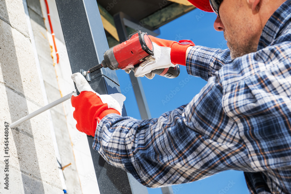 Fototapeta premium Construction Worker Using a Drill to Secure Metal Framing in Bright Daylight Outdoors