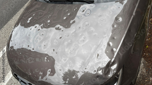 Car hood severely damaged by hail, showing multiple dents and surface imperfections caused by the storm.