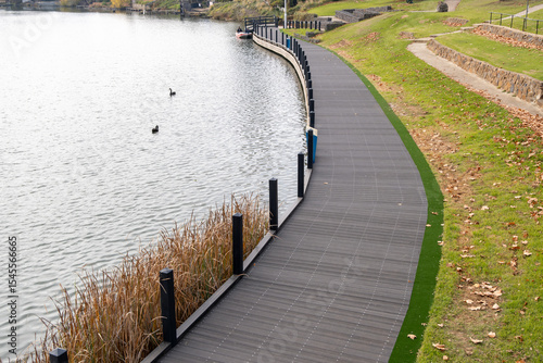 Wallpaper Mural A gently curving lakeside boardwalk lined with posts runs alongside water in an Australian urban park. The design integrates native wetland reeds and grass embankments, a scenic pedestrian walkway. Torontodigital.ca