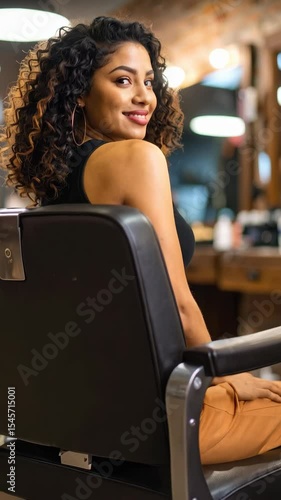 Smiling woman with curly brunette hair sits in styling chair in vintage salon setting