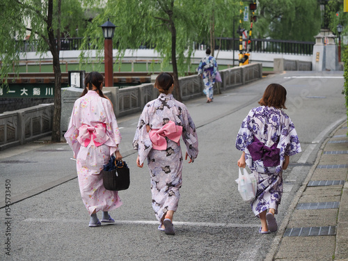 Tourists in bright colorful yukata walking along the Willow-lined canal in Kinosaki Onsen