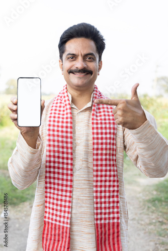 Portrait of smiling mid adult farmer showing smart phone's screen while standing at village.
