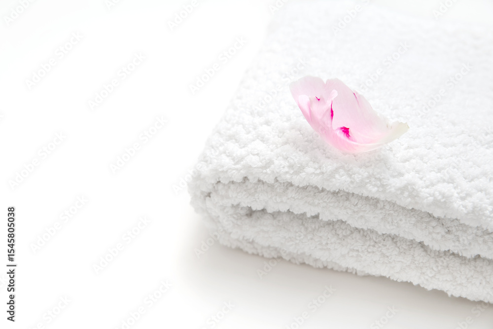 Soft folded towel with pink flower petal on bright white background Soft folded towel with pink flower petal on bright white background