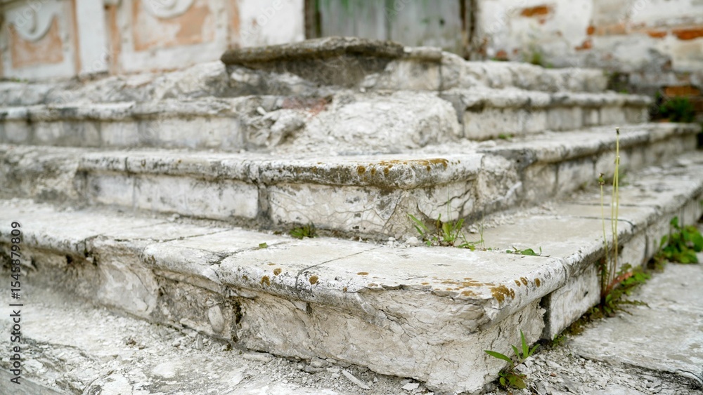 Fototapeta premium Weathered stone steps show signs of age and neglect, with grass and weeds sprouting between the stones