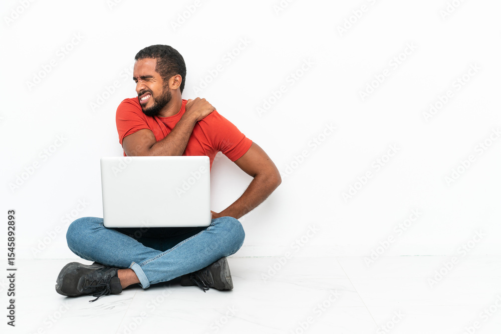 Young Ecuadorian man with a laptop sitting on the floor isolated on white background suffering from pain in shoulder for having made an effort Young Ecuadorian man with a laptop sitting on the floor isolated on white background suffering from pain in shoulder for having made an effort