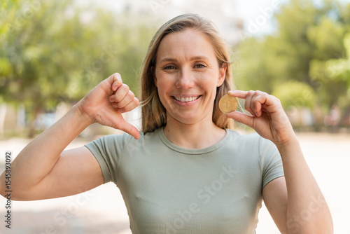 Young blonde woman holding a Bitcoin at outdoors proud and self-satisfied