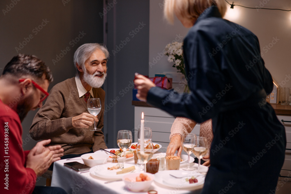 A group of people enjoying a festive dinner at home, sharing laughter and conversation in a warm ambiance. The table is beautifully set with wine glasses, candles, and delicious food. A group of people enjoying a festive dinner at home, sharing laughter and conversation in a warm ambiance. The table is beautifully set with wine glasses, candles, and delicious food.