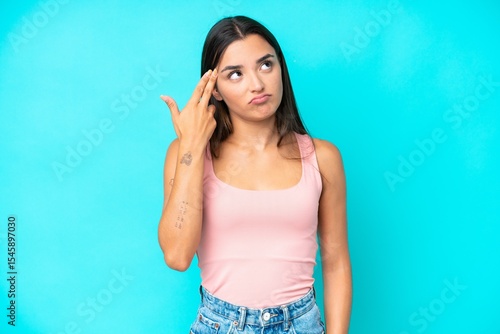 Fototapeta Young caucasian woman isolated on blue background with problems making suicide gesture