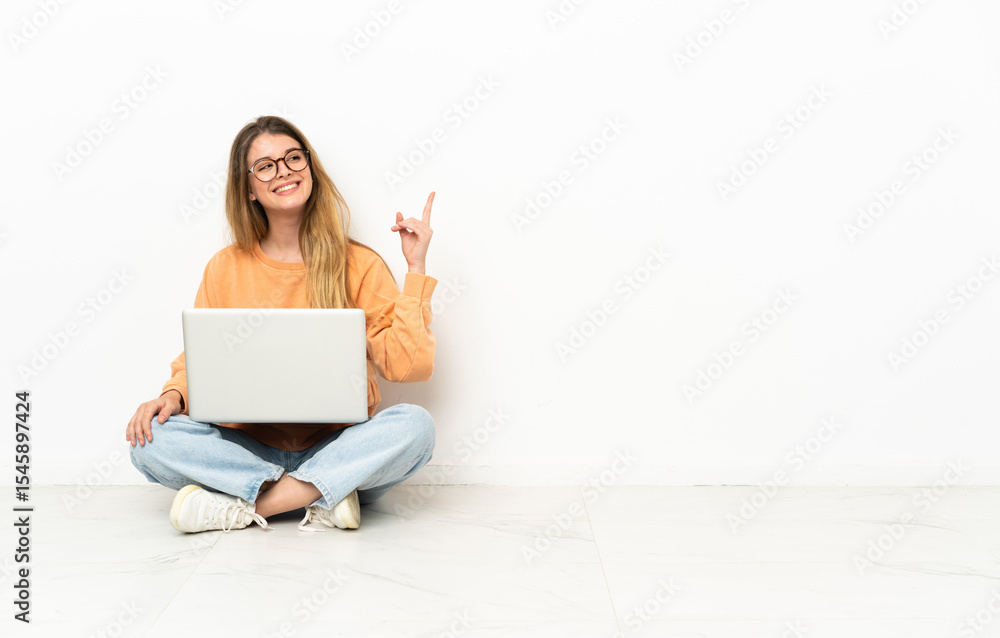 Young woman with a laptop sitting on the floor pointing up a great idea Young woman with a laptop sitting on the floor pointing up a great idea