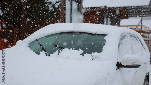 Car wiper blades clean car windows from snow. Snow flakes cover the car with a thick layer.