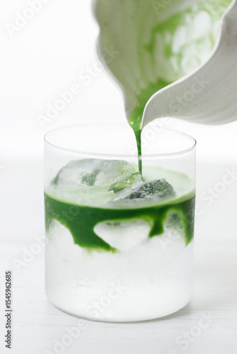 fresh matcha tea, green tea pouring on a glass of coconut water on white wooden table.