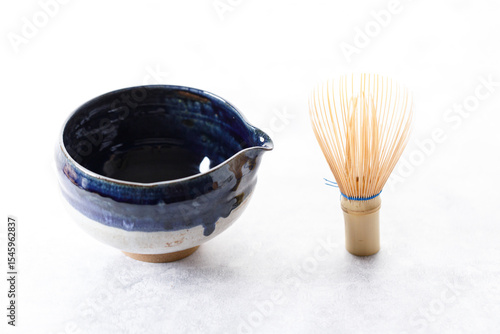Japanese tea bowl glazed with blue and white color and Chasen or Bamboo whisk, an equipment for preparing matcha green tea on white wooden table.