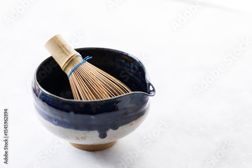 Japanese tea bowl glazed with blue and white color and Chasen or Bamboo whisk, an equipment for preparing matcha green tea on white wooden table.