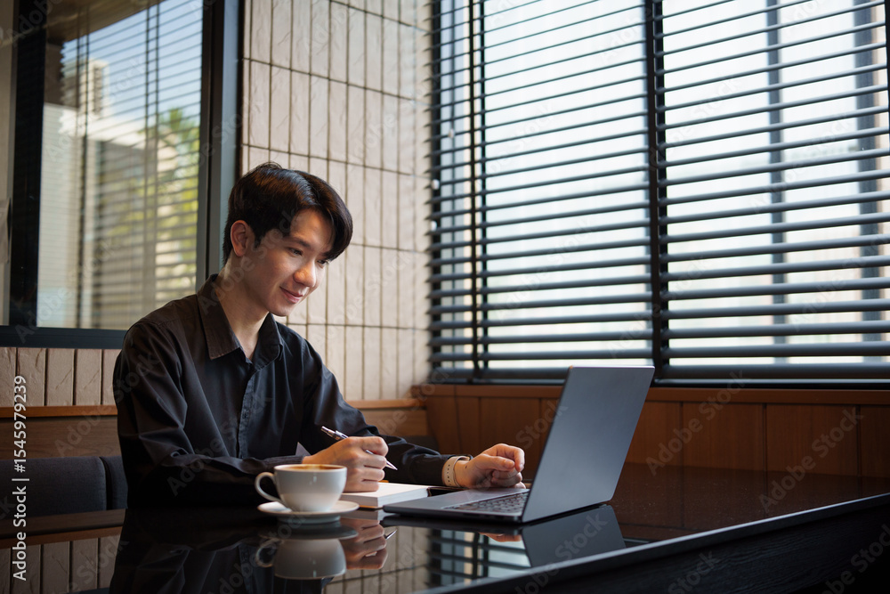 Fototapeta premium Smiling Asian entrepreneur using computer and taking notes in a modern office.